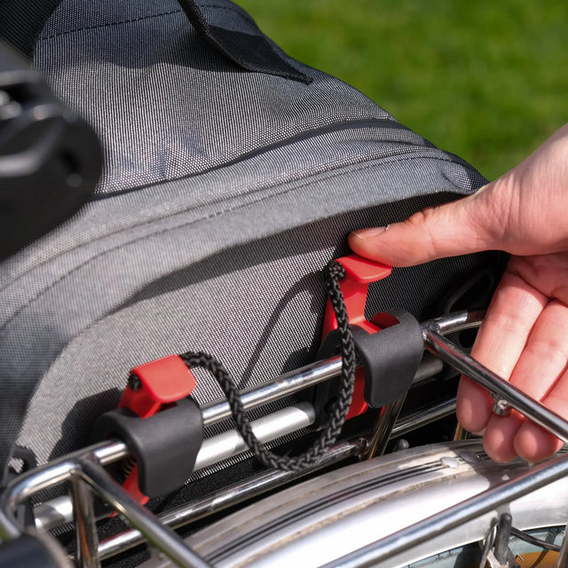 Person securing a pannier backpack 2.1 plus onto a bike rack with a blurred green background