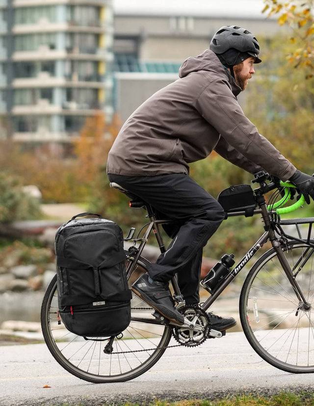 Man biking in the rain with the Two Wheel Gear Duffle bag on the rack of his bike.